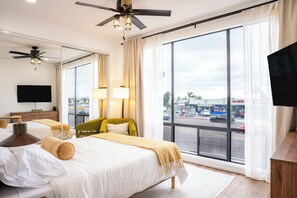 Ett hotellrum med ett stort fönster, en säng, en stol, en tv och en takfläkt.