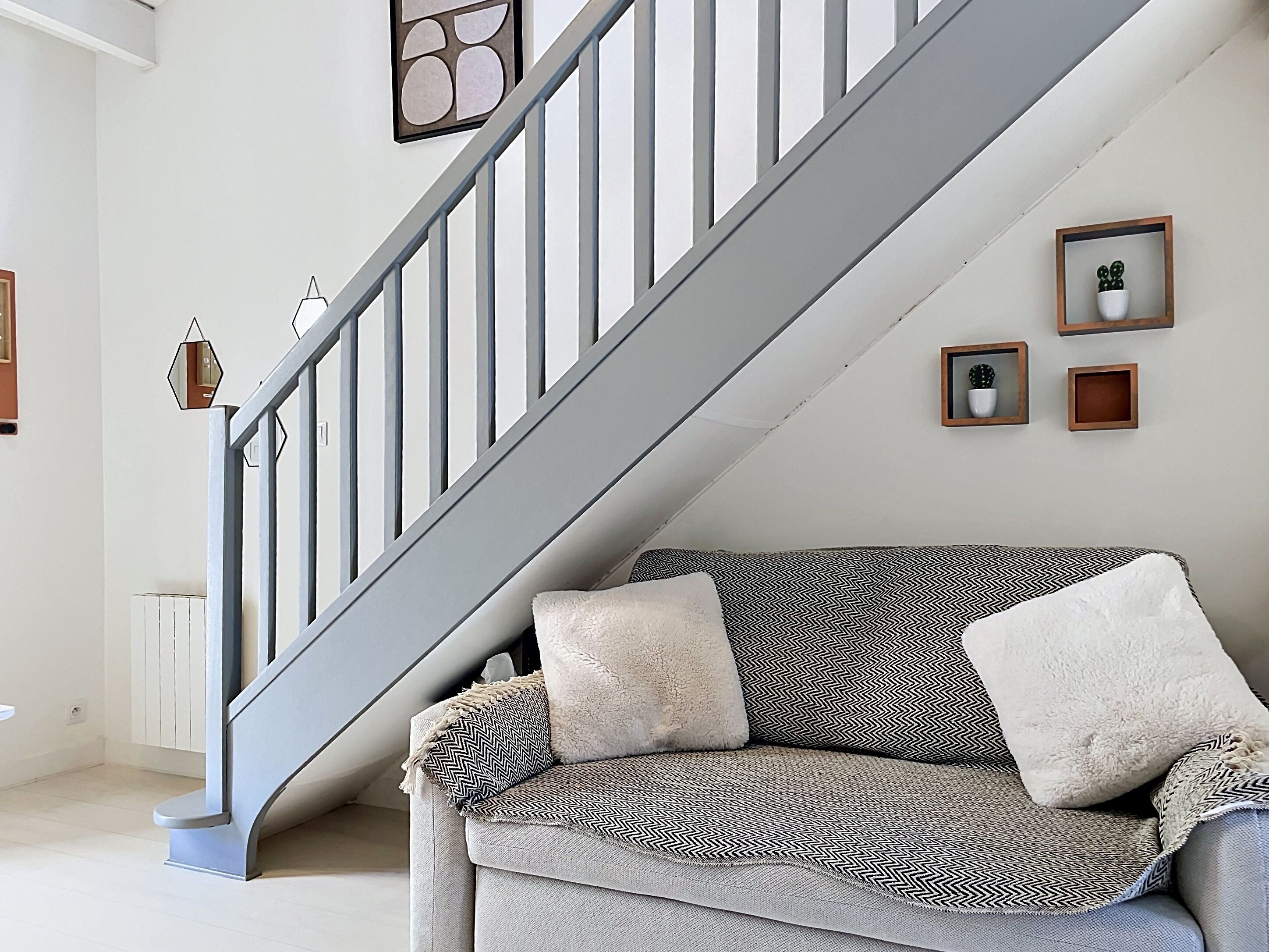 Una escalera con barandilla gris, un sofá gris con cojines estampados y un radiador blanco.