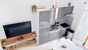 A modern kitchen with a flat-screen TV, wooden shelves, and a dining area with a table and chairs. - Village house within walking distance of shops and sea (le barcares)