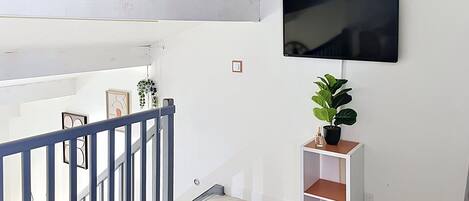 Un interior moderno con una escalera, un televisor montado y una planta en maceta.