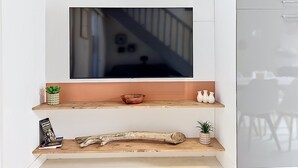 A modern interior with a mounted TV, wooden shelves, decorative items, and a staircase in the background. - Village house within walking distance of shops and sea (le barcares)