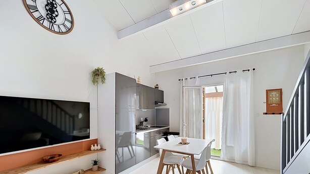 A modern living room with a flat-screen TV, a dining table with chairs, a staircase, and a kitchen area. - Village house within walking distance of shops and sea (le barcares)