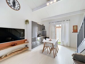 En moderne stue med et fladskærms-tv, et spisebord med stole, en trappe og et køkkenområde.