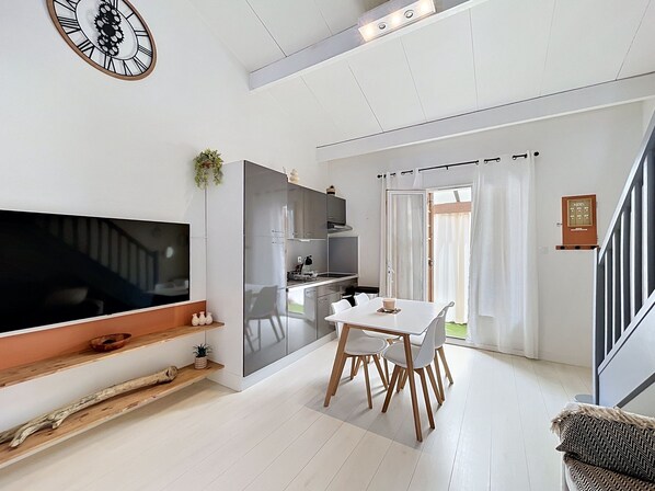 Ein modernes Wohnzimmer mit Flachbildfernseher, einem Esstisch mit Stühlen, einer Treppe und einer Küchenzeile.
