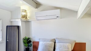 A bedroom with a bed, pillows, a potted plant, an air conditioning unit, and a door. - Village house within walking distance of shops and sea (le barcares)