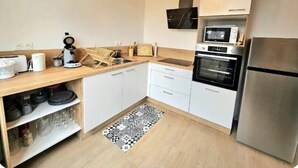 Moderni keittiö, jossa on valkoiset kaapit, ruostumattomasta teräksestä valmistettu jääkaappi, mikroaaltouuni ja kahvinkeitin.