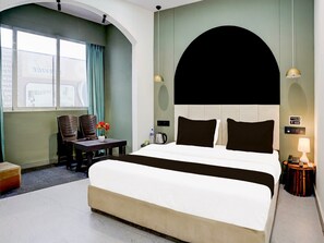 Ein Hotelzimmer mit einem großen Bett, einem Schreibtisch mit Stühlen, einer Kaffeemaschine und Blick ins Freie.