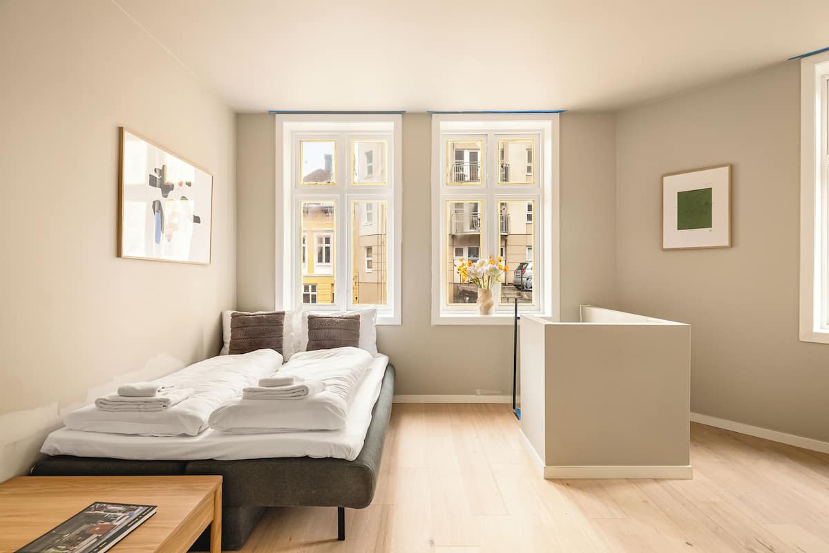 A modern hotel room with a bed, bedside table, and a window with a view of buildings.
