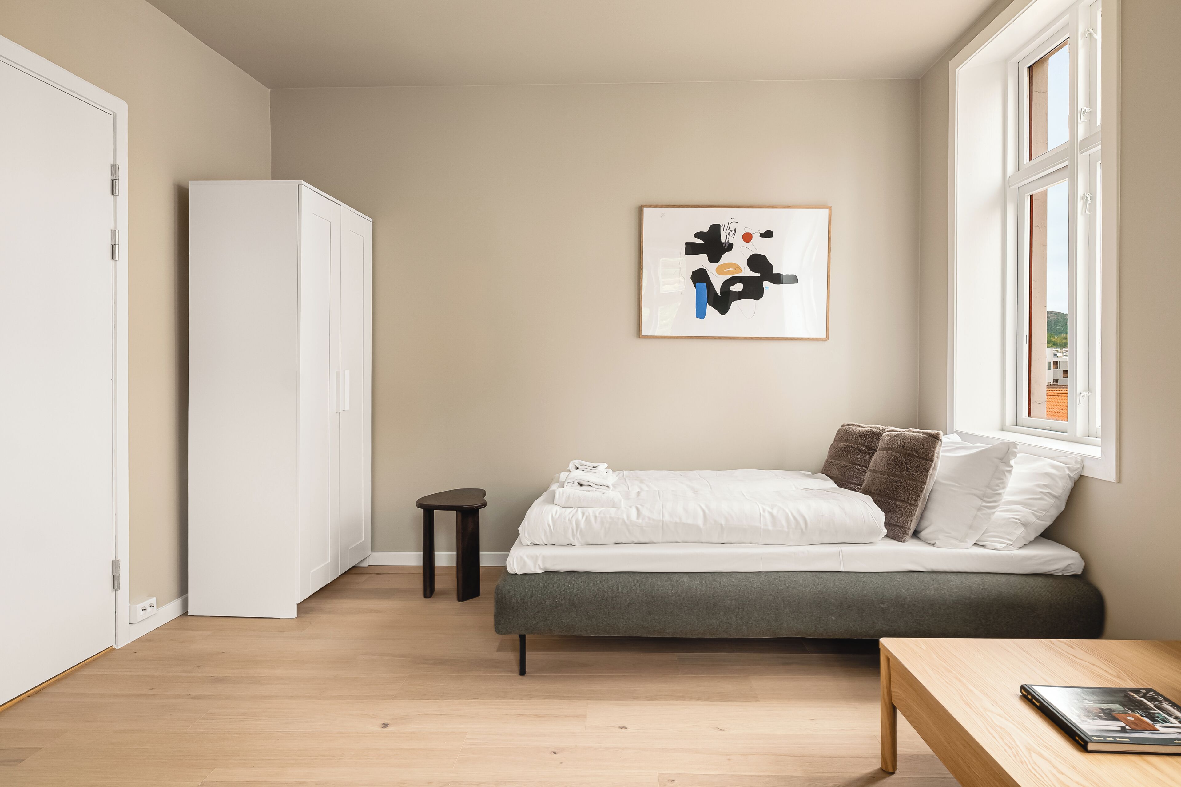 Une chambre à coucher avec un lit, une petite table, une armoire et une fenêtre donnant sur un beau paysage.