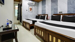 Hotelkamer met twee bedden, een plafondventilator, een airconditioner, een bureau met waterkoker en een raam met gordijnen.