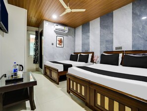 A hotel room with two beds, a ceiling fan, an air conditioning unit, a desk with a kettle, and a window with curtains. - Deluxe Hotel O Madhapur VIP Hills (Hyderabad)