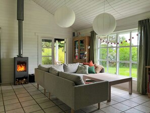 A living room with a fireplace, a sofa, a table, and a view of greenery outside. - Summer house with path to pier by fjord (Skibby)
