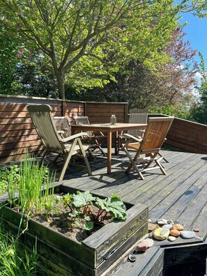 Eine Holzterrasse mit Tisch und Stühlen, umgeben von einem Holzzaun und Grünpflanzen.