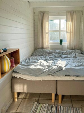 Ein Zimmer mit Bett, einem Vorhangfenster, einem Regal mit Dekoration und einem kleinen Tisch.