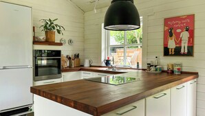 Una cocina con encimera de madera, armarios blancos, una lámpara colgante negra y un cartel en la pared.