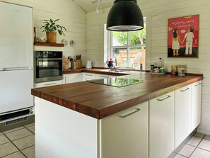 A kitchen with a wooden countertop, white cabinets, a black pendant light, and a poster on the wall. - Summer house with path to pier by fjord (Skibby)