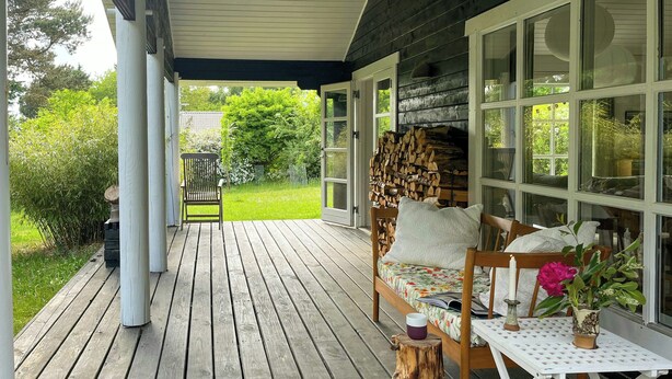 Una terraza de madera con un sofá, una mesa, una silla y una pila de leña.