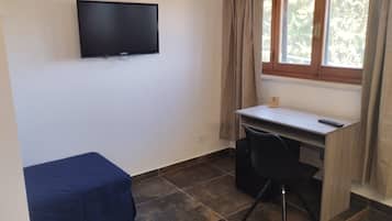 A small room with a bed, a desk, a chair, a TV mounted on the wall, and a window with curtains.