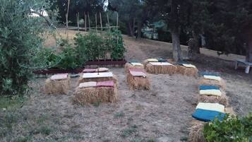 Un jardín con fardos de heno dispuestos en círculo, rodeado de árboles y un banco de madera.