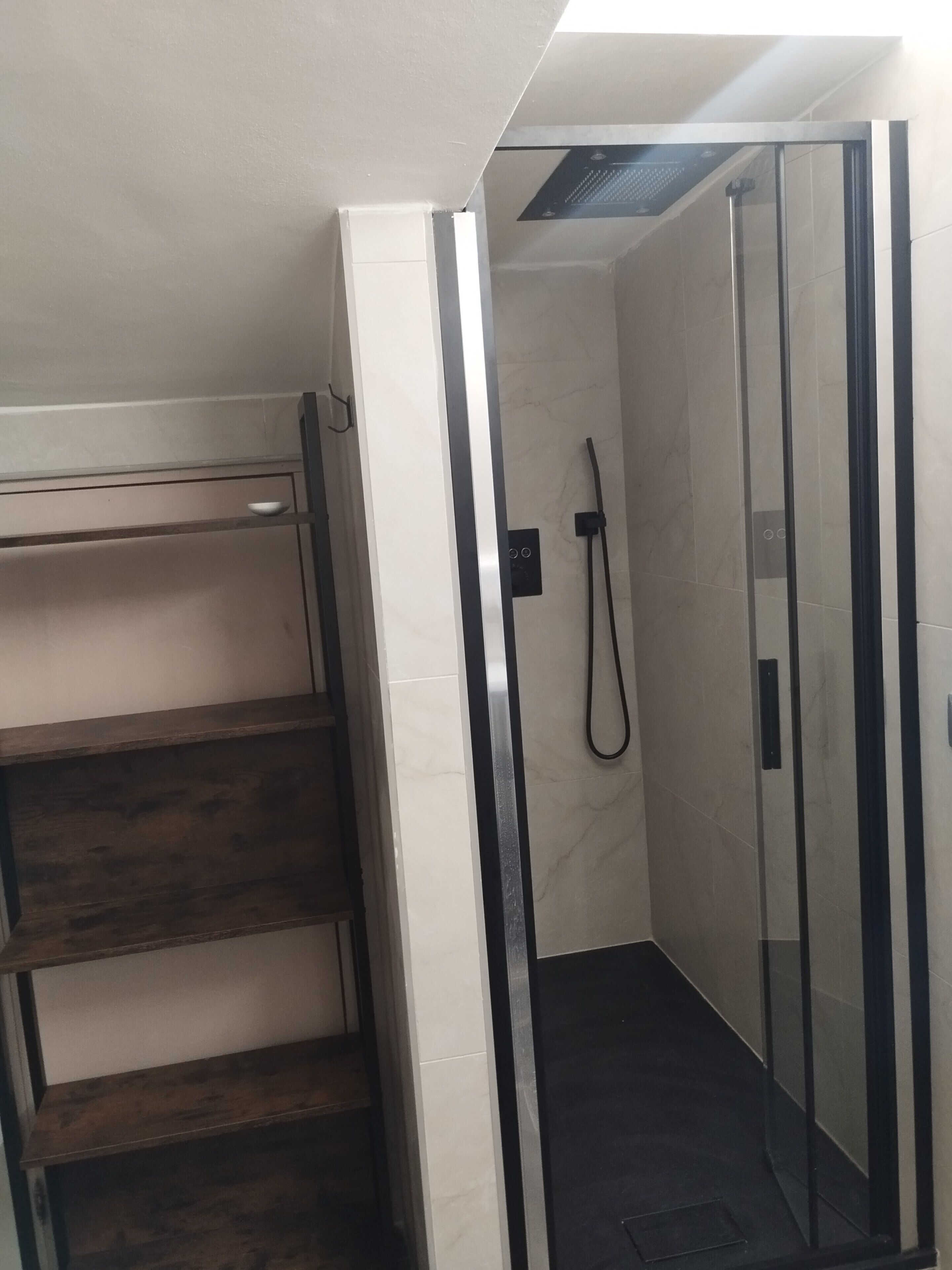 Eine Dusche mit Glastüren, einem Holzregal und einer gefliesten Wand.