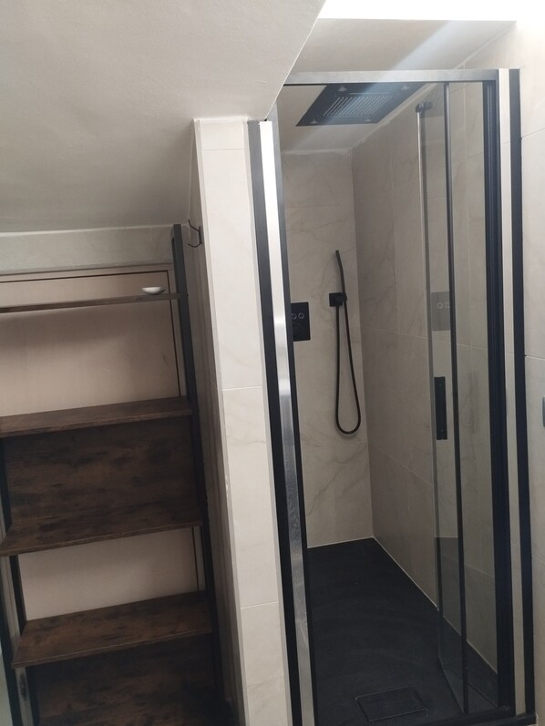 A shower with glass doors, a wooden shelf, and a tiled wall.