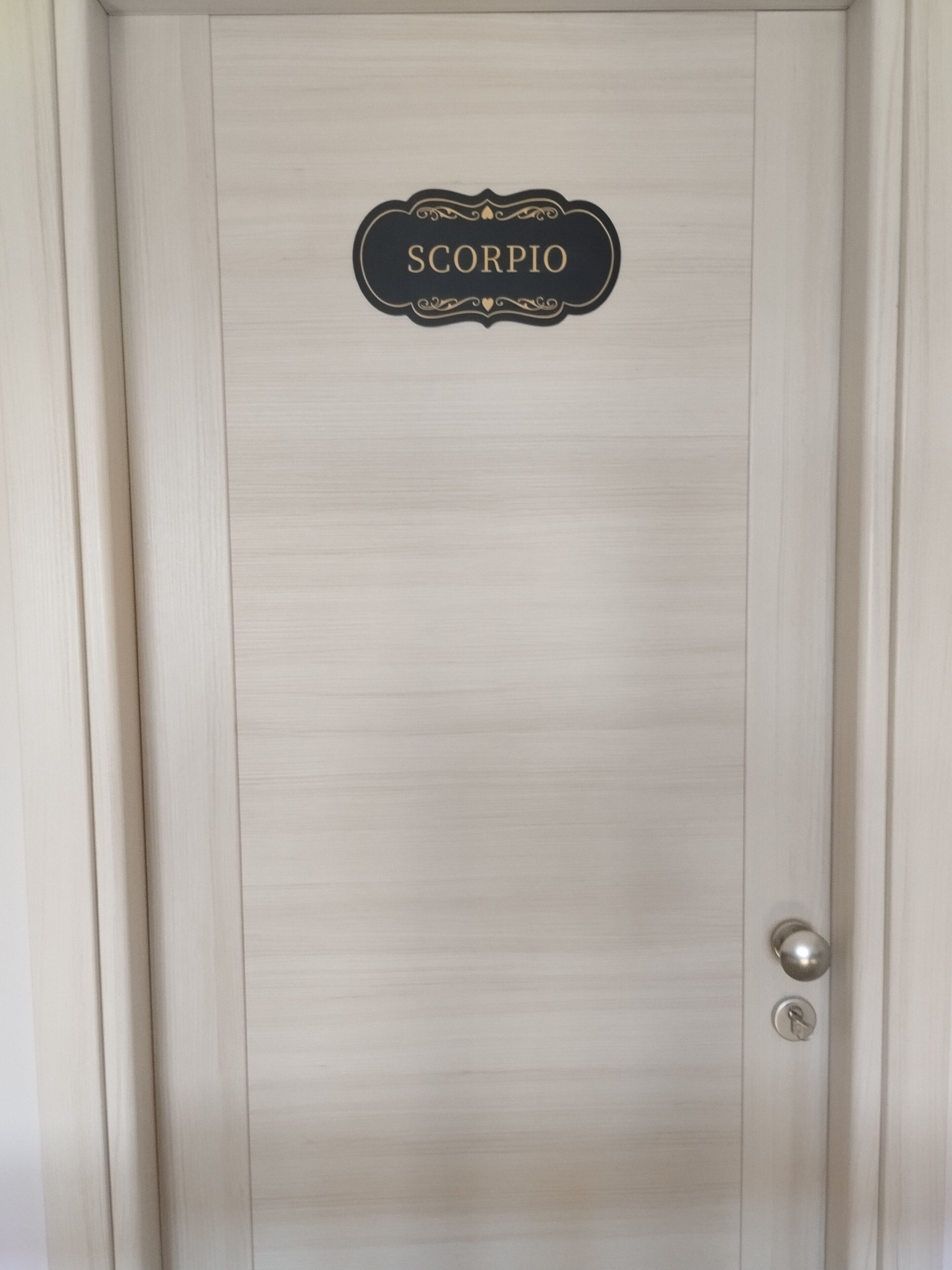 Een deur met een naambordje waarop 'SCORPIO' staat en een sleutelgat.