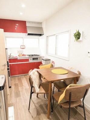 Une cuisine de taille réduite avec des meubles rouges, une cuisinière et un coin repas comprenant une table et des chaises en bois.