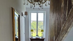 Un pasillo con piso de madera, un candelabro, un espejo, una mesa con lámparas y una escalera.