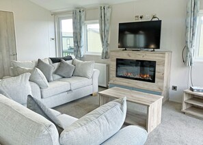 A living room with a sofa, television, fireplace, and windows. - Clearwater Pet Friendly (No Hot Tub) (Hexham)