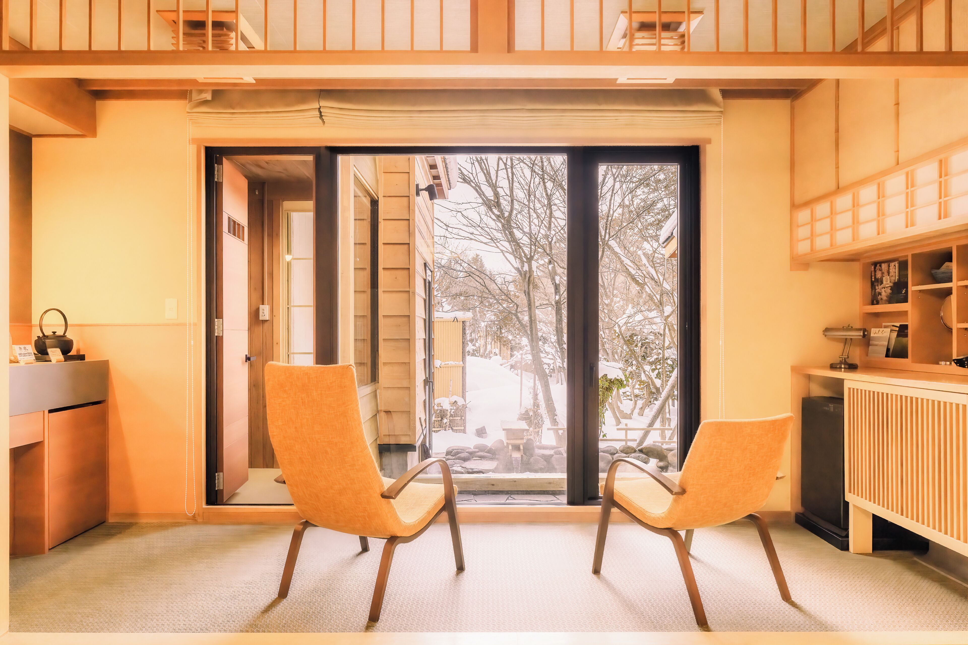 A room with two chairs, a desk, and a view through a glass door to an outdoor area with a bench and trees.