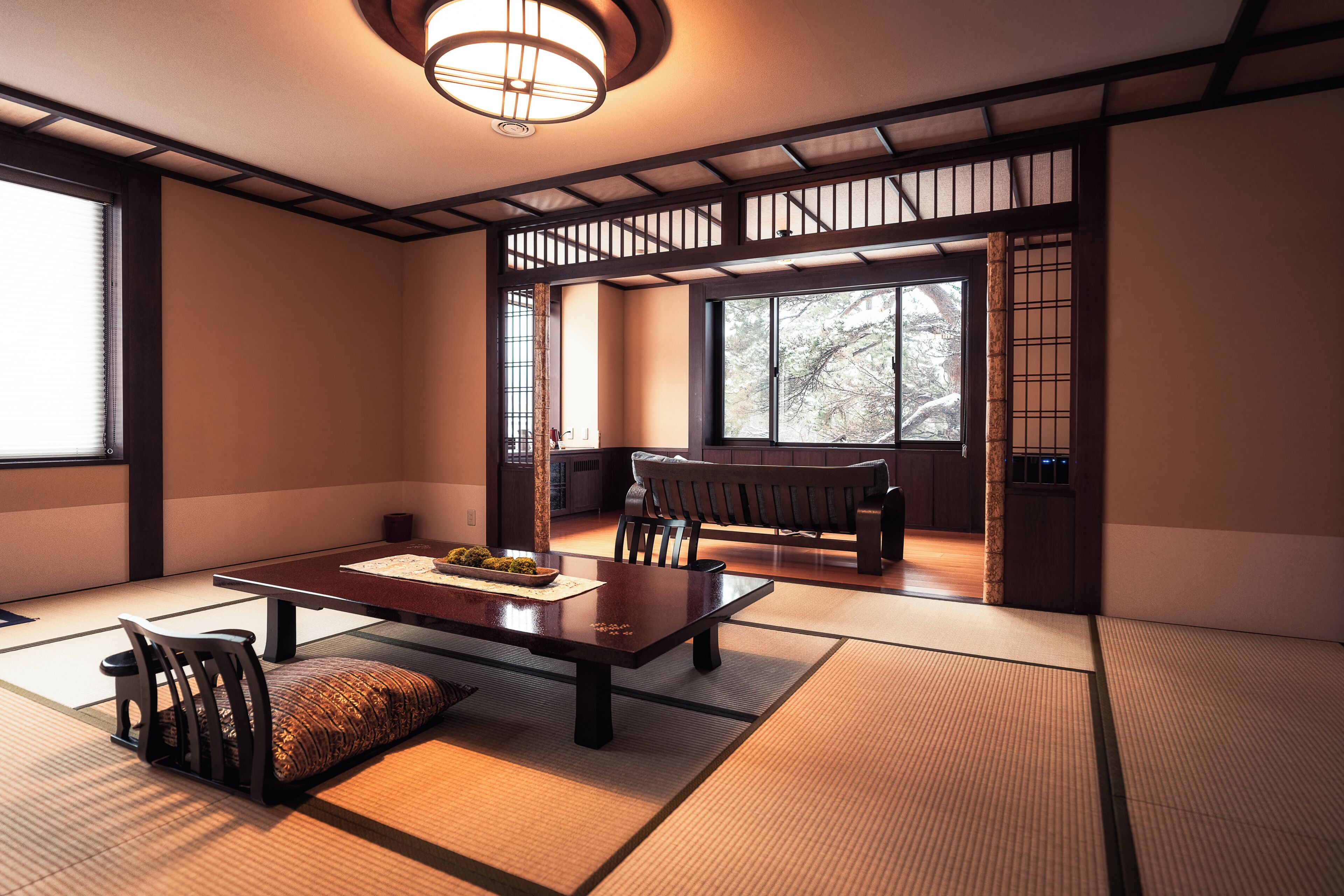 Une pièce de style japonais traditionnel, avec un sol recouvert de tatamis, une table basse, des chaises et une porte coulissante donnant sur une autre pièce.