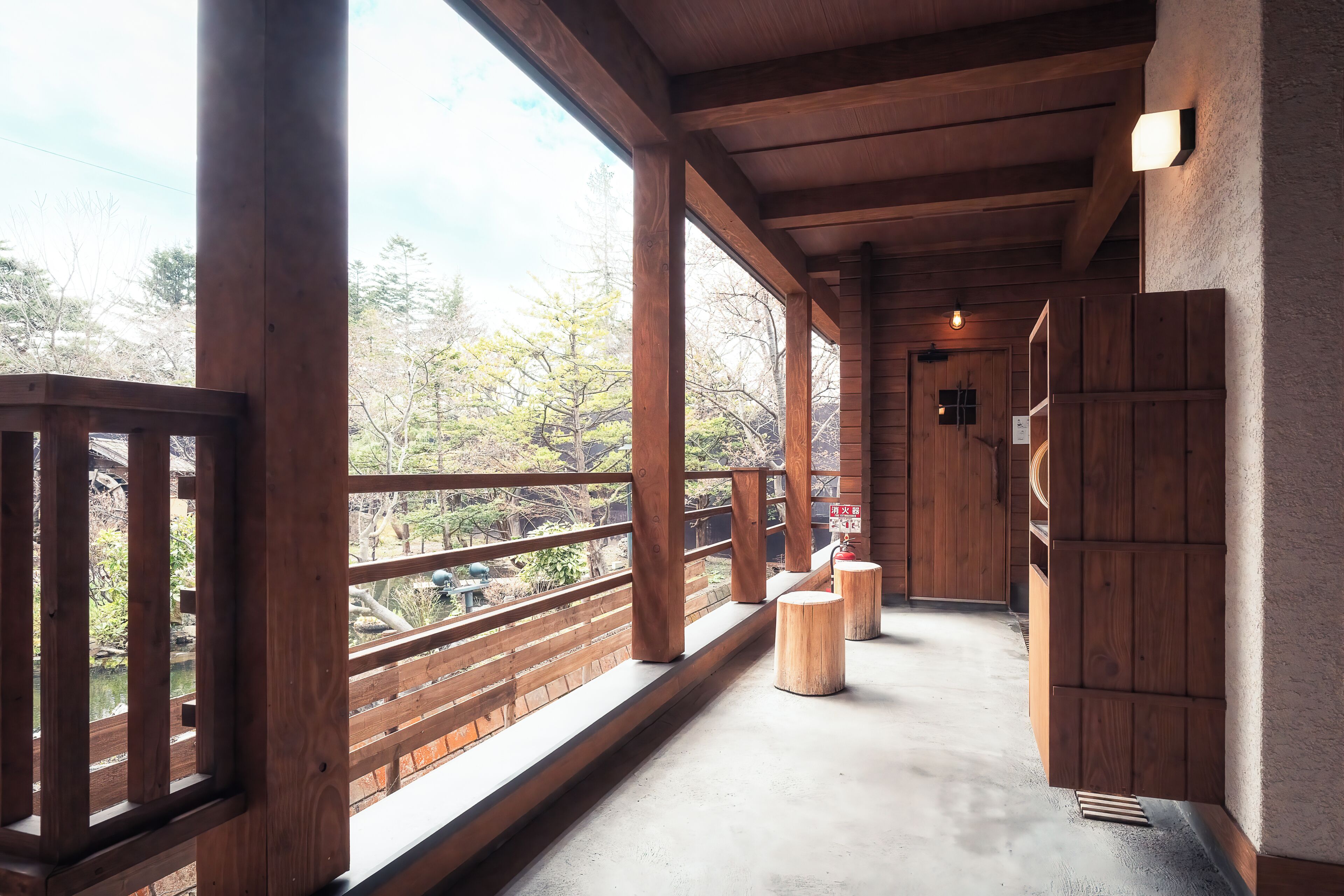 A wooden corridor with a balcony, wooden railings, and a view of trees.