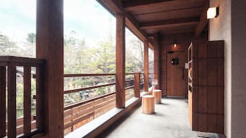 A wooden corridor with a balcony, wooden railings, and a view of trees.