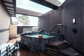 Ein Whirlpool mit Steinsäulen, einer Holzterrasse und einer Metalltreppe, die hinaufführt.