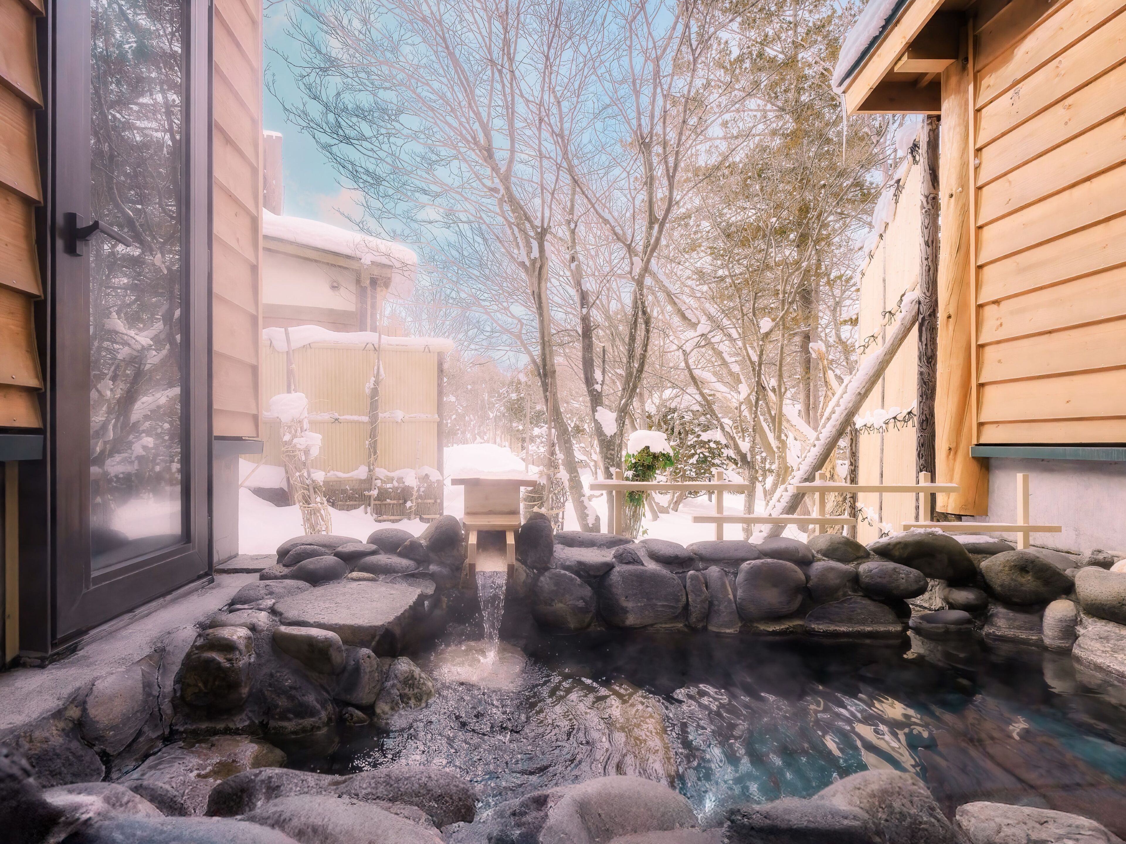A stone hot spring surrounded by rocks and wooden structures.