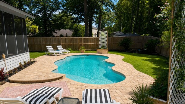 Un jardin avec une piscine, des chaises longues, une petite table et un pot de fleurs.
