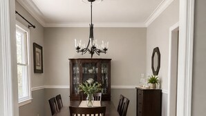 Une salle à manger avec une table en bois, des chaises, un lustre, un buffet contenant de la verrerie et un miroir au mur.