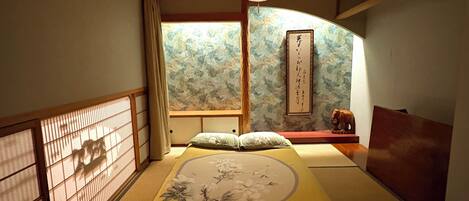 A traditional Japanese room with tatami flooring, a low wooden bed, a hanging lamp, and a shoji screen.
