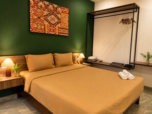 Une chambre d’hôtel avec un lit, des lampes de chevet, un téléviseur fixé au mur, un miroir, une étagère avec des serviettes et un mur vert.