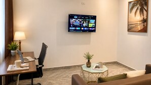 A hotel room with a desk, chair, laptop, air conditioning unit, TV, and a painting of a beach scene. - Peaceful Studio near Hoi An Old Town - Pool & Working Space (Đà Nẵng)