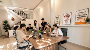 A modern meeting room with a wooden table, chairs, laptops, and a staircase in the background. - Peaceful Studio near Hoi An Old Town - Pool & Working Space (Đà Nẵng)