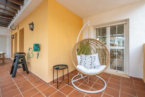 Eine Terrasse mit Korbstuhl, einem kleinen Tisch, einer Trittstufe und einem an der Wand montierten Telefon.