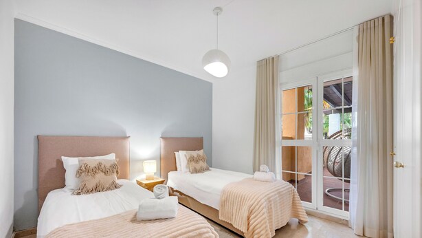 Habitació d'hotel amb dos llits, una finestra gran amb cortines, una làmpada al sostre i vista exterior.