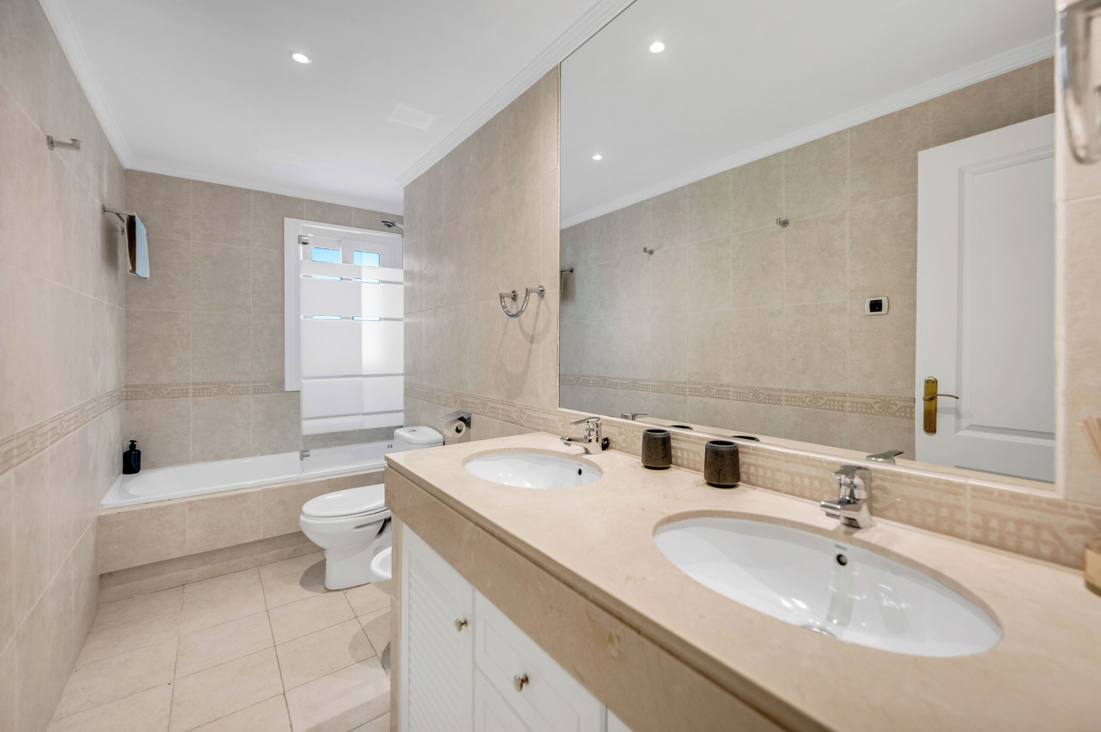 A modern bathroom with two sinks, a bathtub, a toilet, and a large mirror.