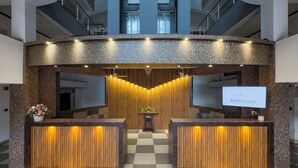 Una reception d'albergo con pavimento a scacchi, parete in pannelli di legno e uno schermo televisivo che mostra il nome dell'hotel.