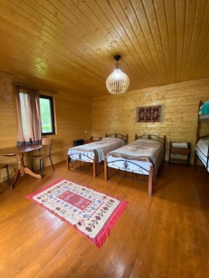 A wooden cabin room with two beds, a dining table, and a hanging light fixture.