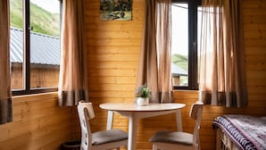Habitación de cabaña de madera con una mesa redonda, dos sillas, una cama con un edredón estampado y un cuadro en la pared.