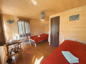 A wooden cabin with two single beds, a small table with chairs, a kettle, and a hanging light fixture.