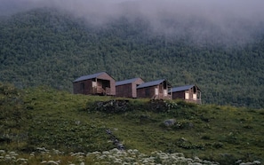 A row of rustic cabins on a hillside with a forest backdrop.