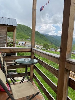 A wooden deck with a table and chairs, overlooking a green valley and mountains.